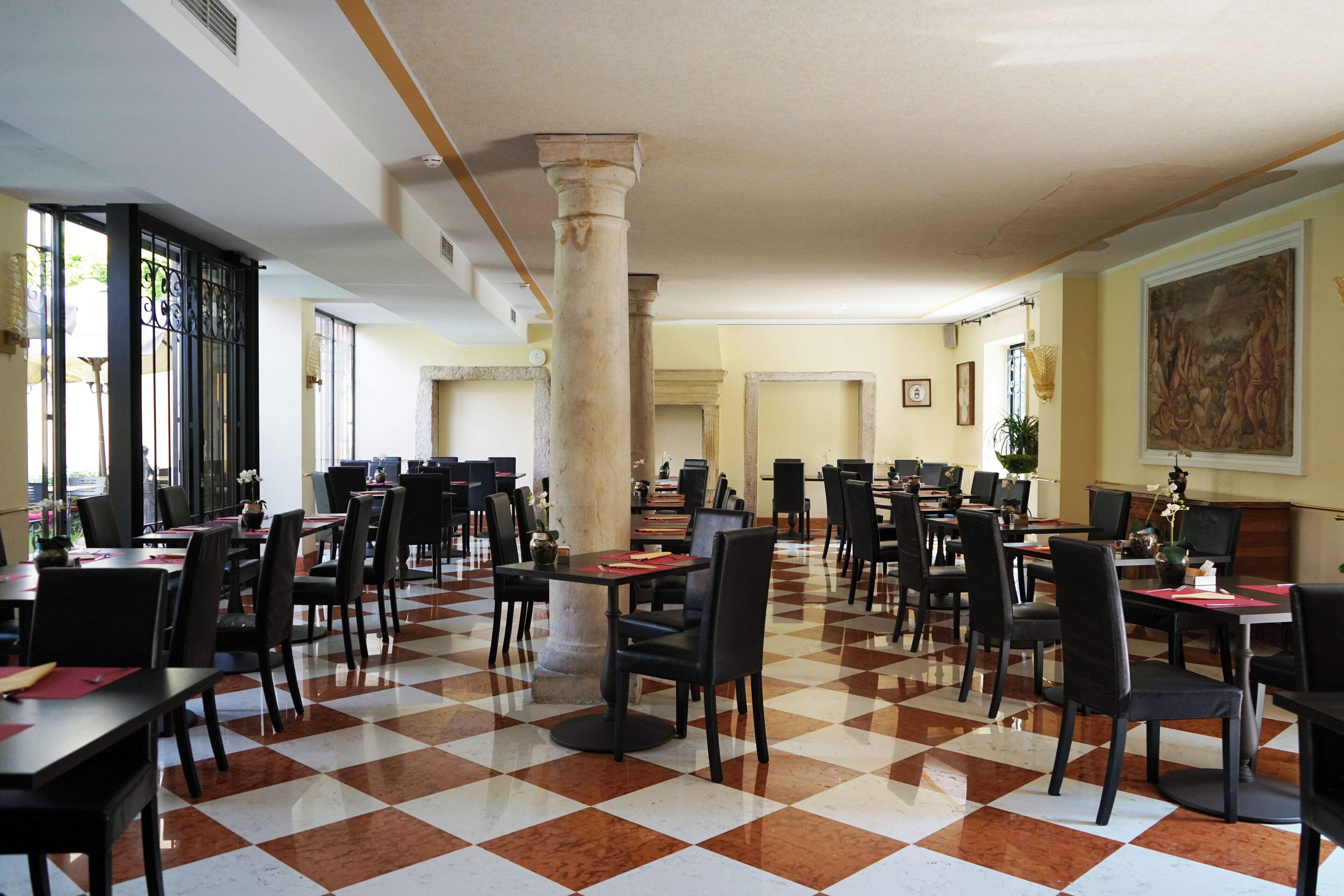 A spacious dining area with checkered flooring, multiple tables and chairs, and a central column.