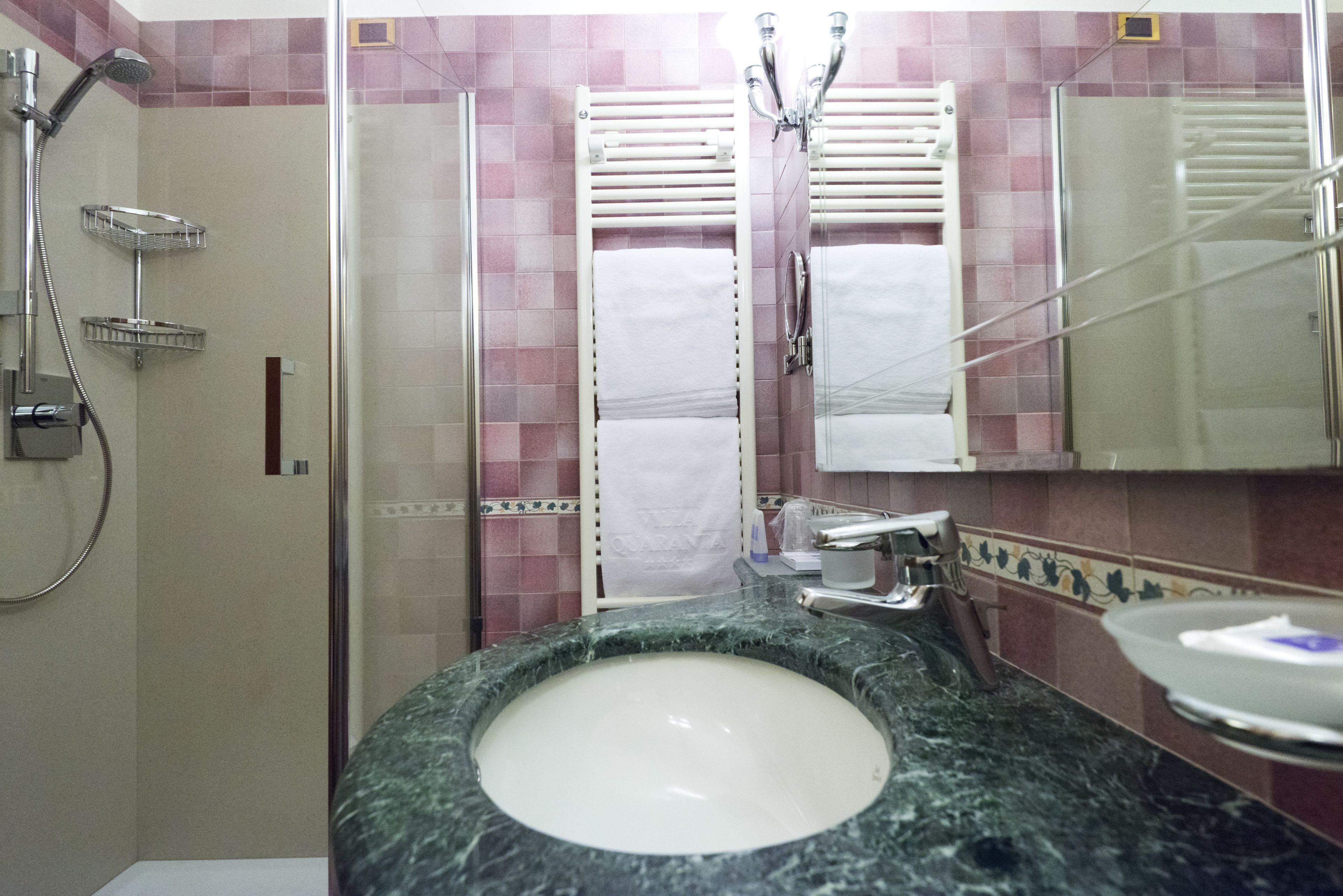 Un baño con lavamanos de mármol, cabina de ducha con mampara de vidrio y toallero.