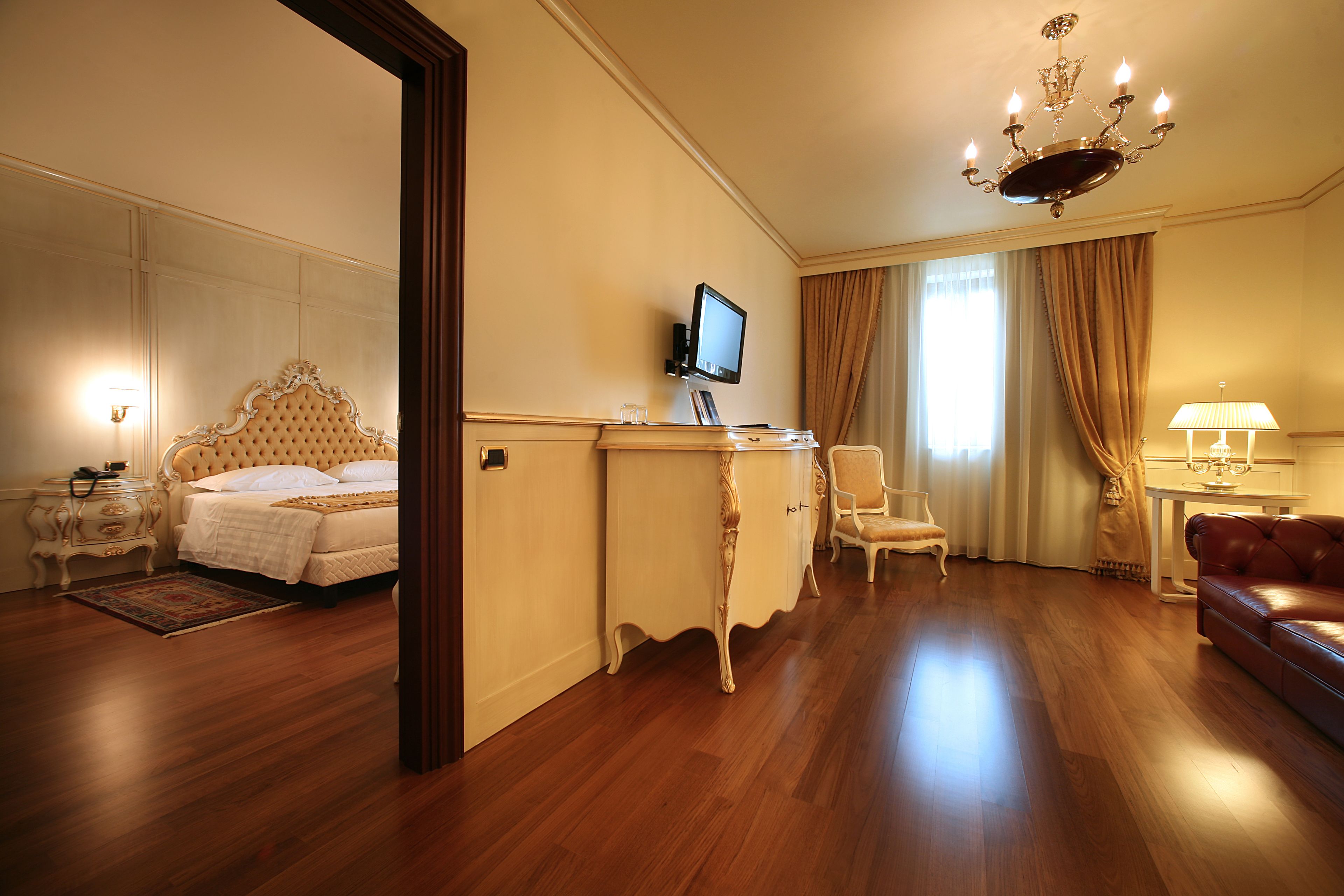 Camera d'albergo con un letto, una scrivania, una sedia, un divano in pelle e un lampadario.