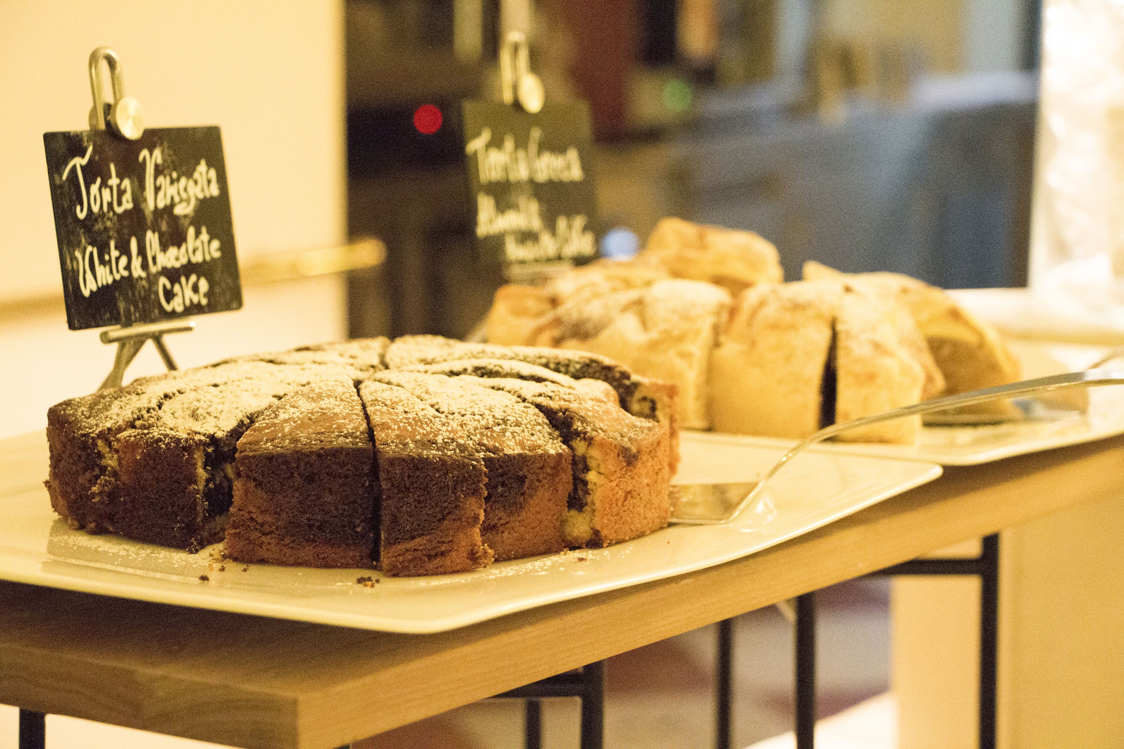 Esposizione di torte bianche e al cioccolato, con un cartello che indica 'Torta di Pasticceria White & Chocolate Cake'.