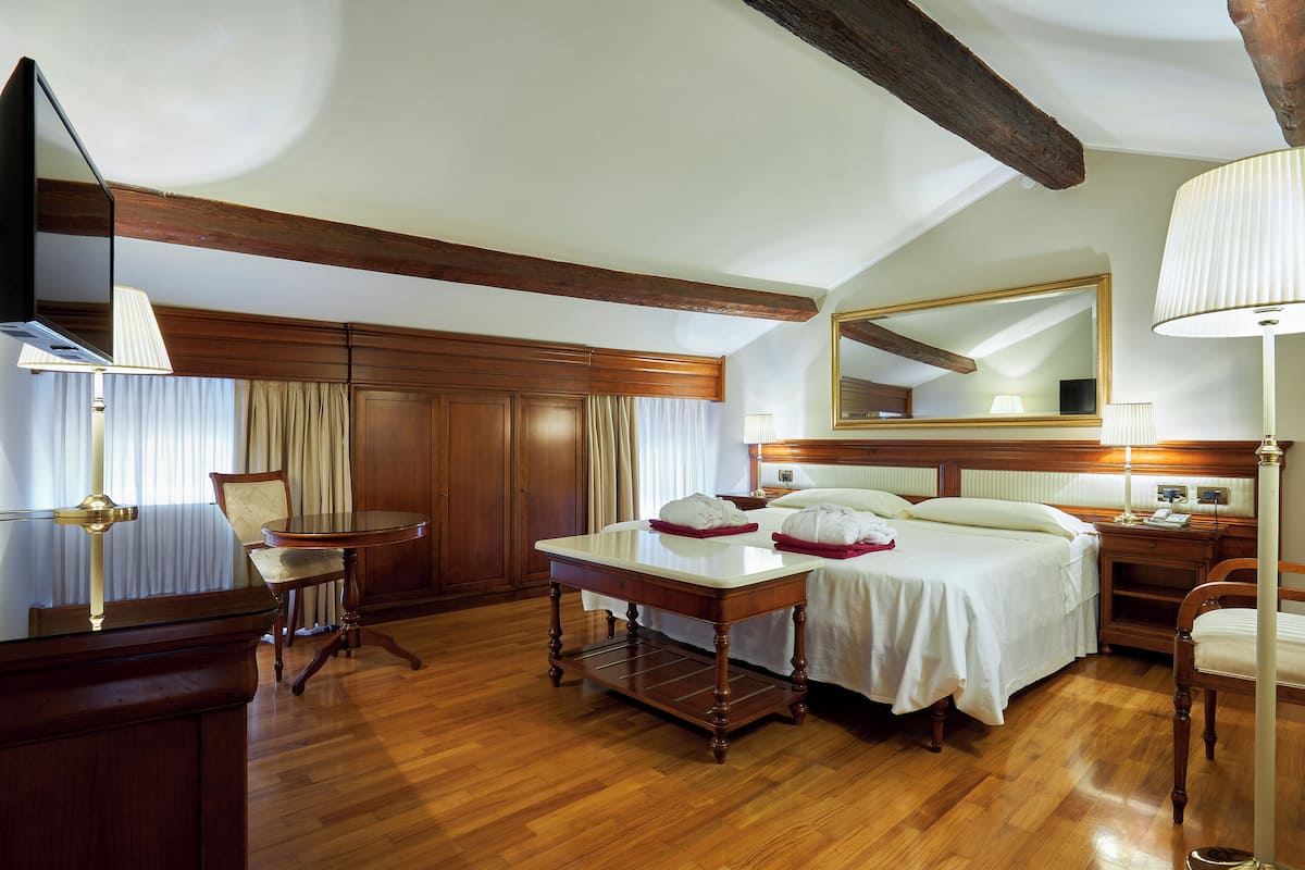 Une chambre d’hôtel avec un plancher en bois, un lit avec du linge de lit blanc, un bureau avec une lampe et un grand miroir au mur.