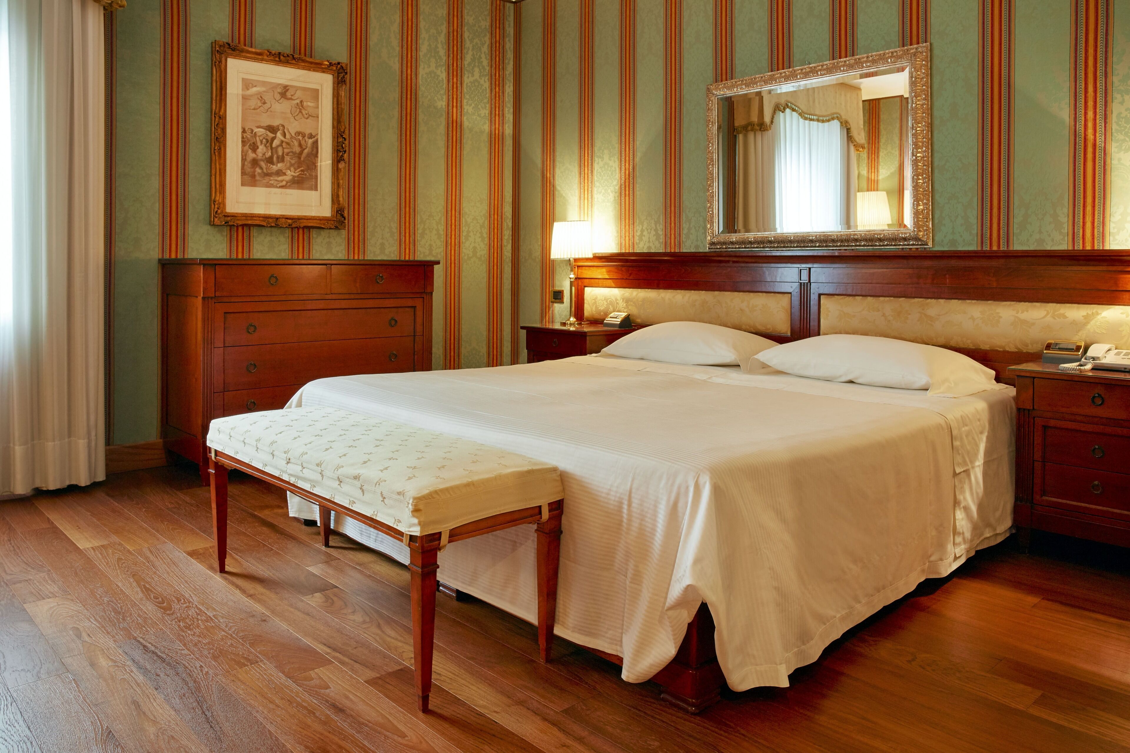 Una camera d'albergo con un letto grande, mobili in legno, un comodino, uno specchio e un quadro appeso alla parete.