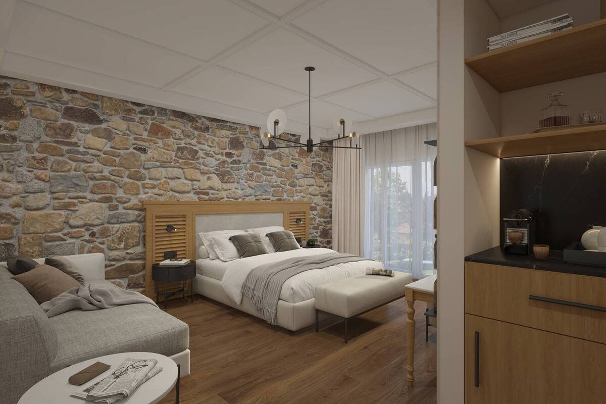 Une chambre avec un mur en pierre, une tête de lit en bois, une table de chevet, une commode, un lit avec des oreillers, un banc, une petite table ronde avec un journal et une armoire en bois.