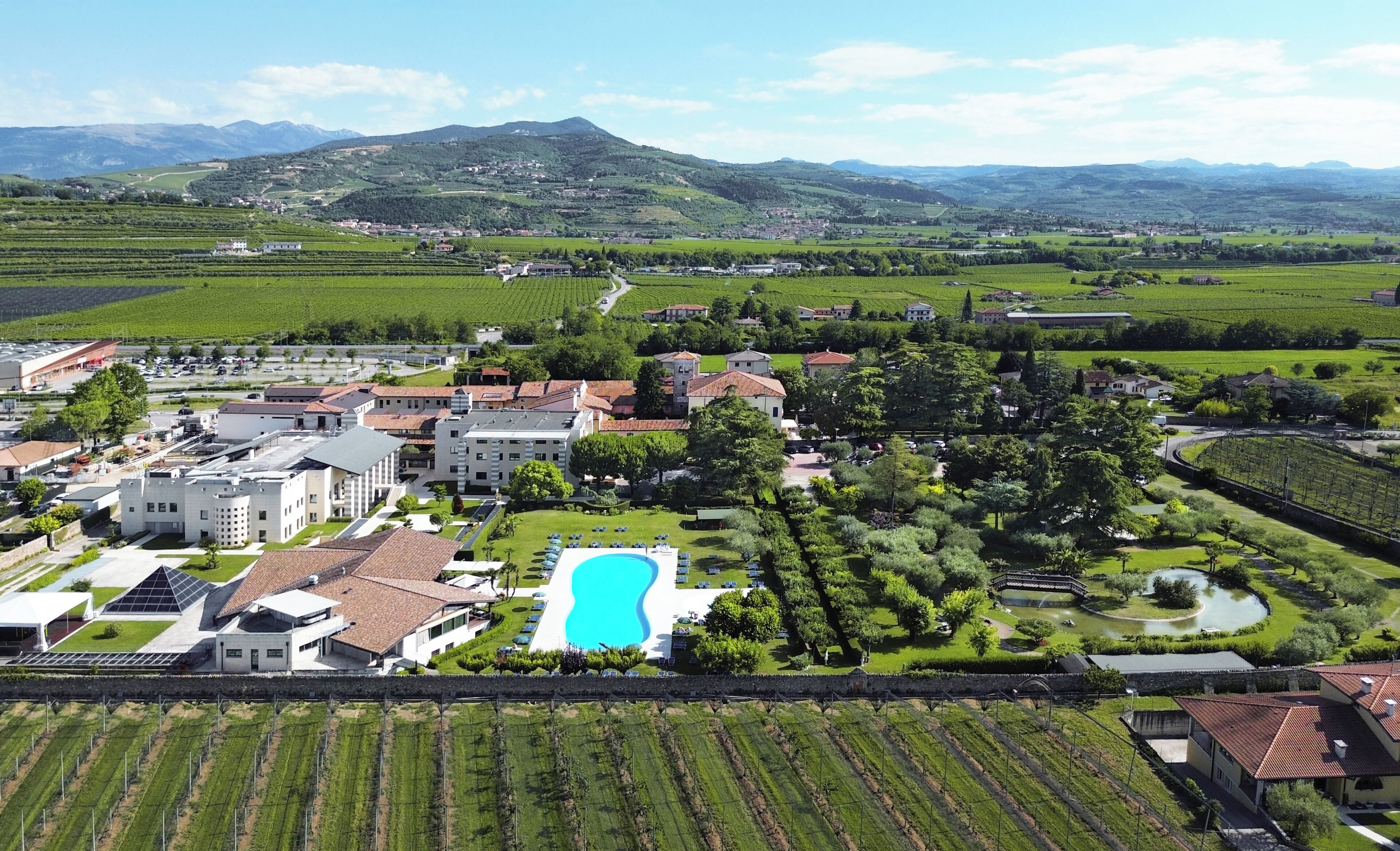 Uma grande propriedade com piscina, vinhedos e montanhas ao fundo.