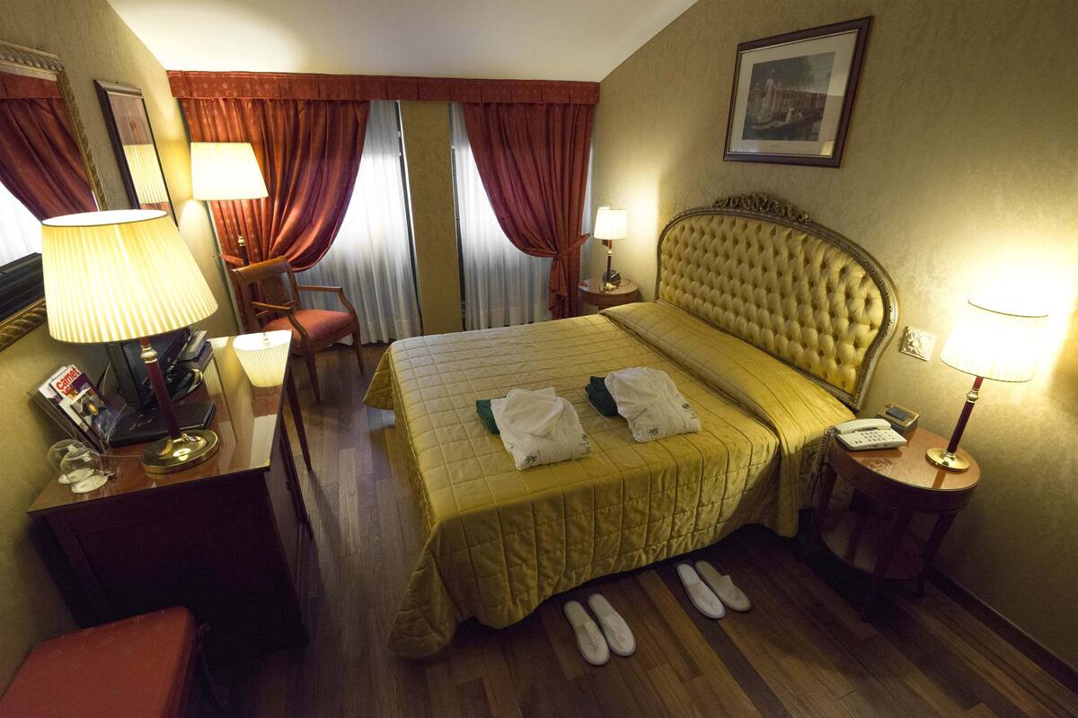 Une chambre d’hôtel avec un grand lit, deux lampes de chevet, une chaise, un bureau avec une lampe et un téléphone.
