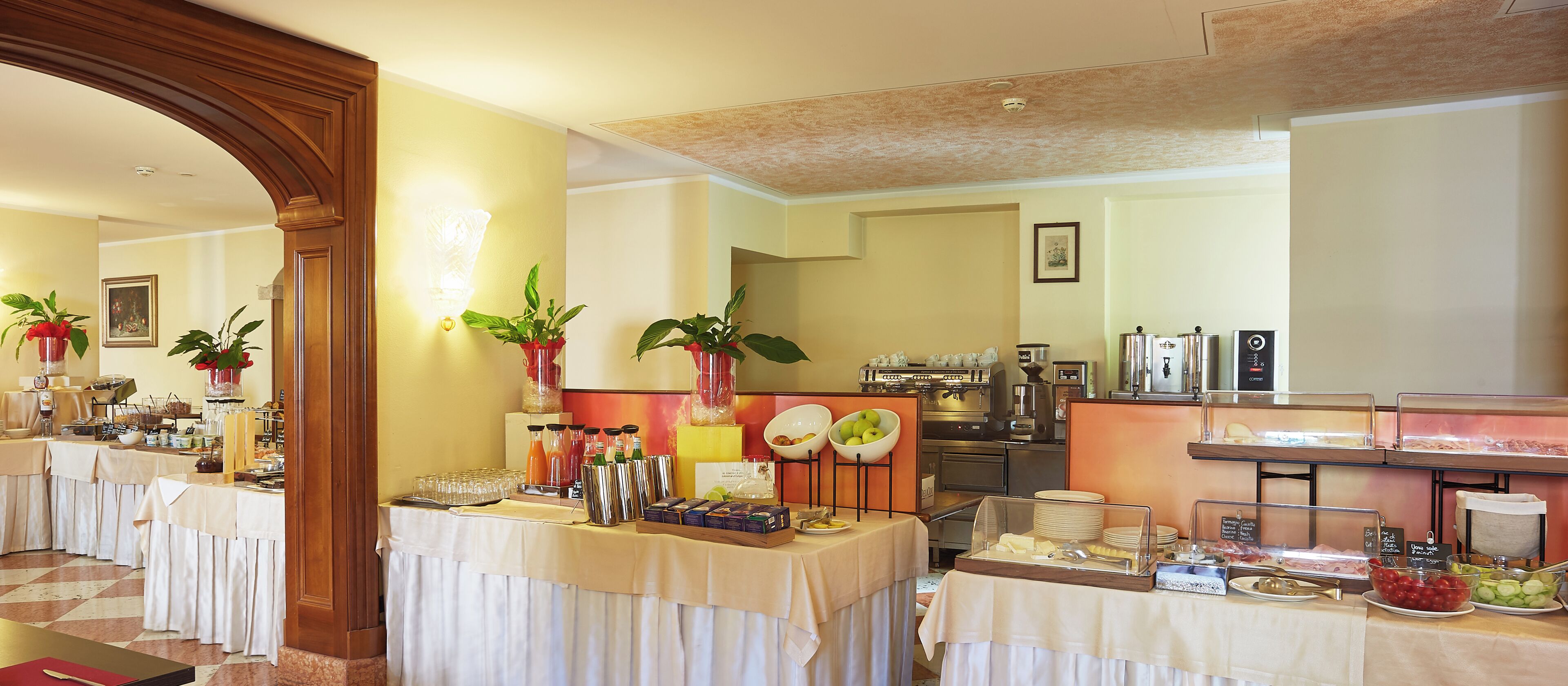 A buffet setup with various food items and beverages, a coffee machine, and a seating area with tables.