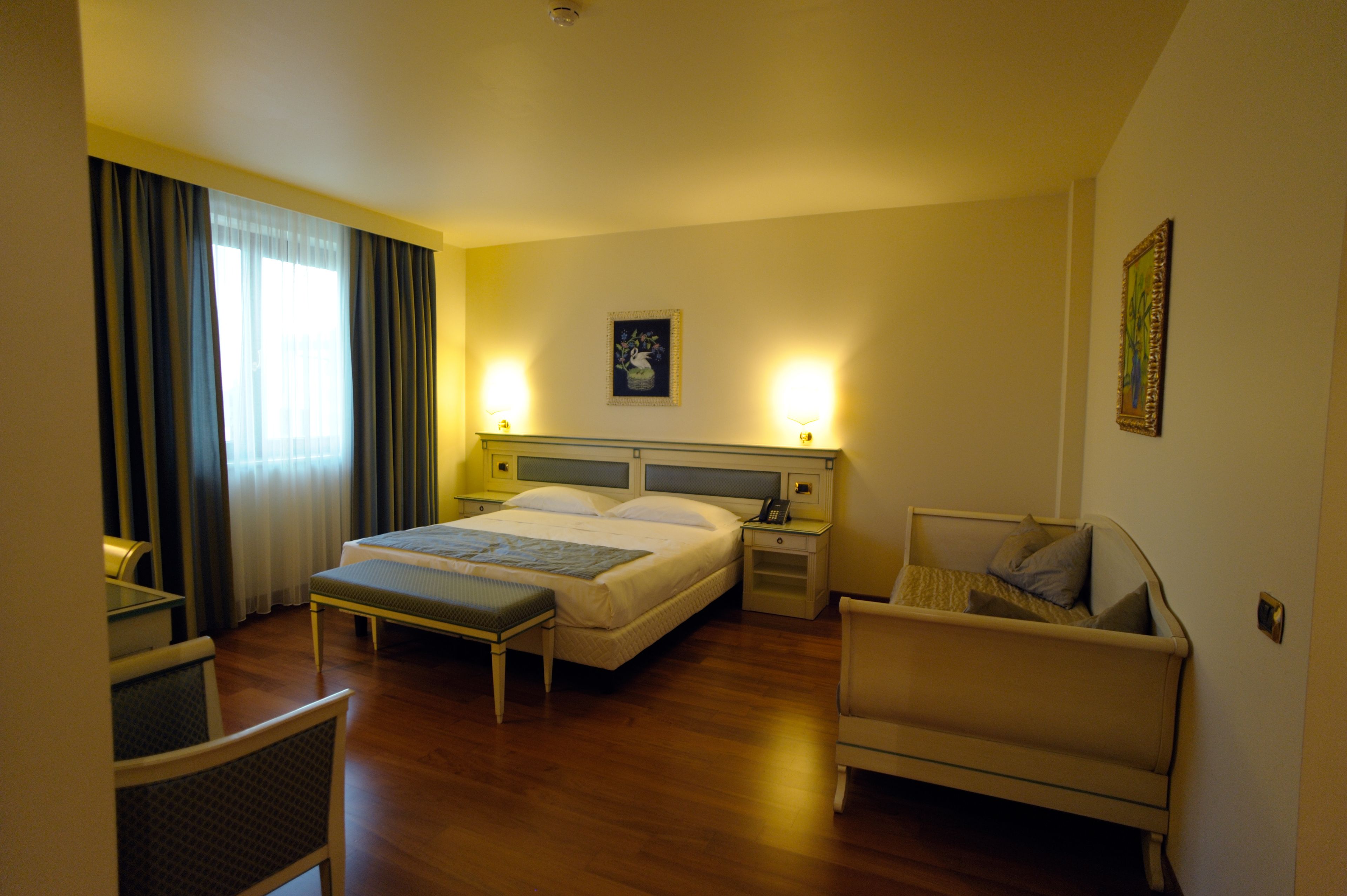Habitación de hotel con cama, mesitas de noche, una silla, escritorio y ventana con cortinas.