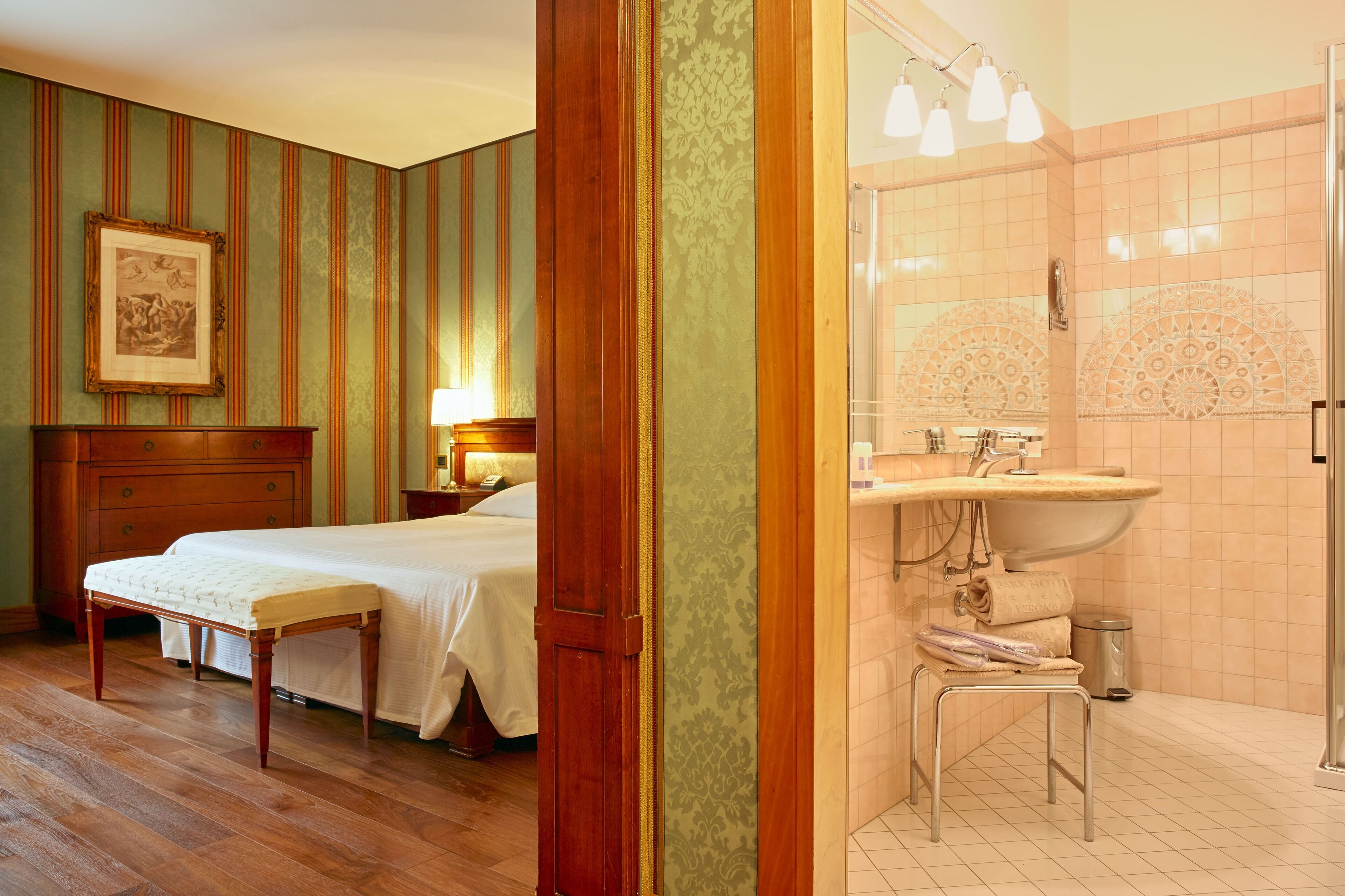 A hotel room with a bed, bedside table, lamp, and a bathroom with a sink and mirror.