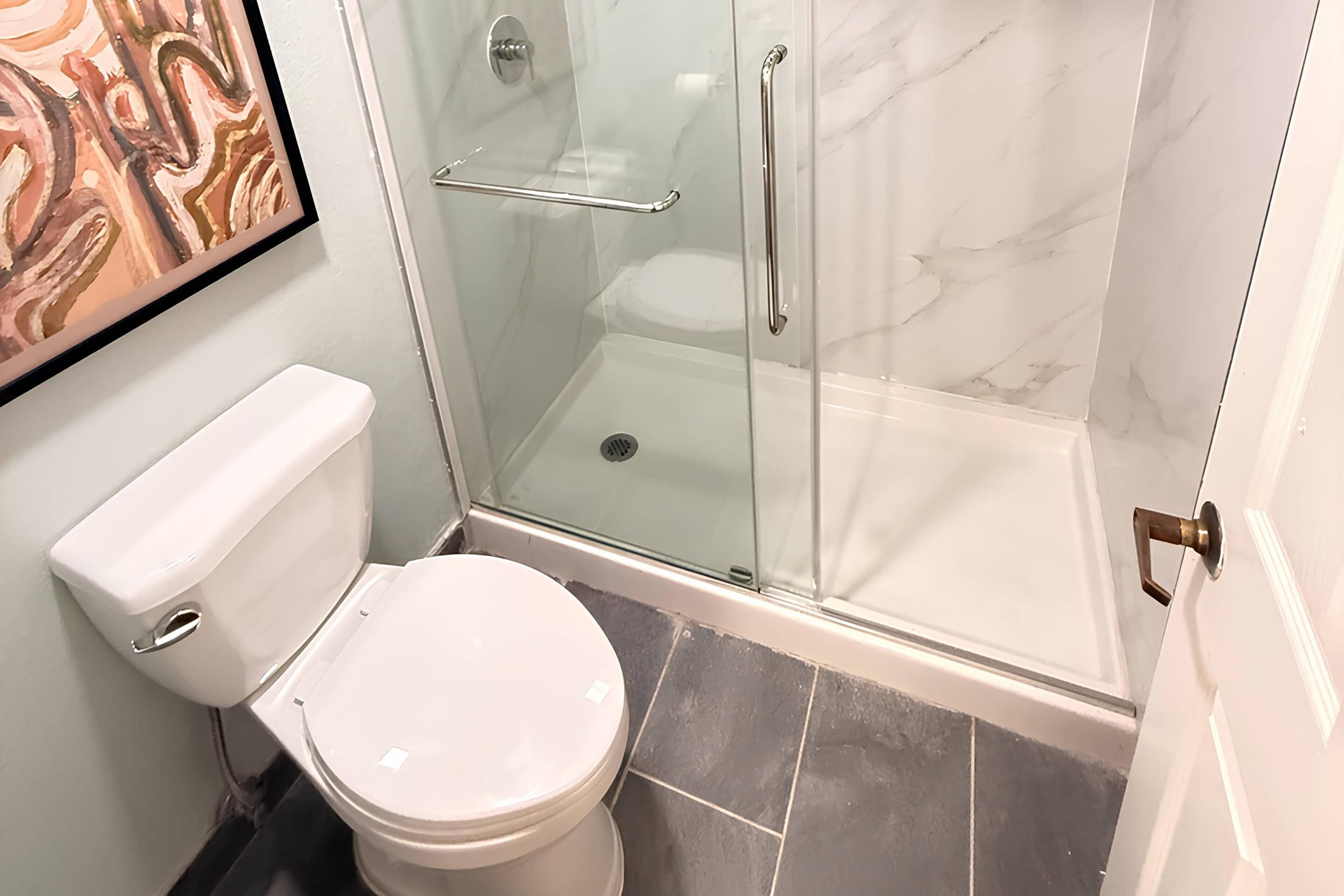 A bathroom with a toilet, a glass shower enclosure, and a marble-tiled floor.
