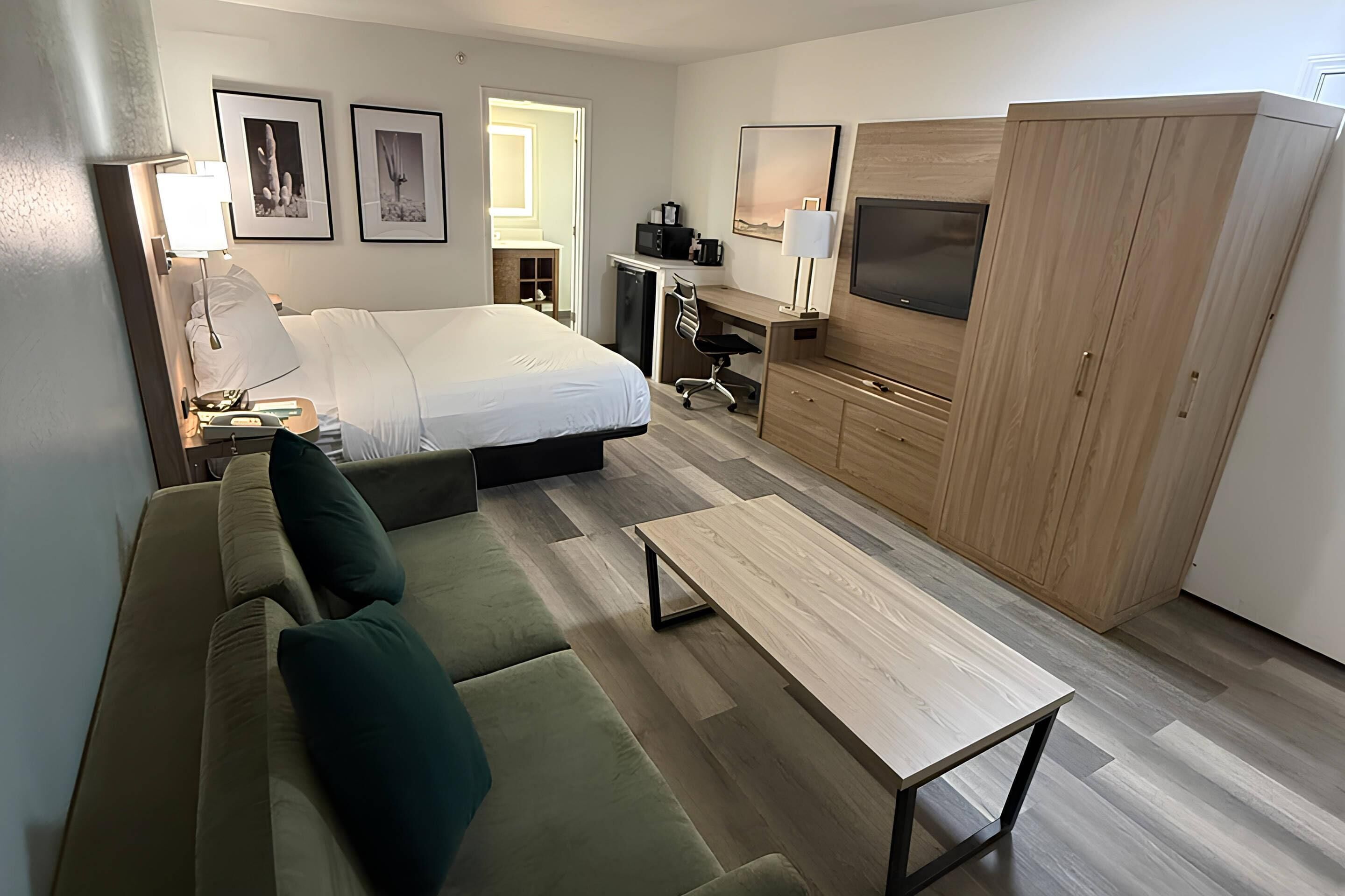 Habitación de hotel compacta con cama, sofá, escritorio, televisor y armario.