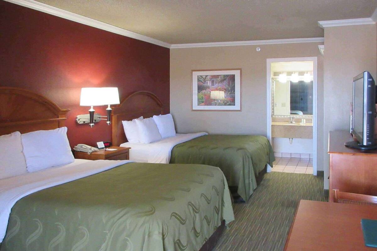Habitación de hotel con dos camas, un escritorio, televisión y baño con espejo. También hay un cuadro en la pared.