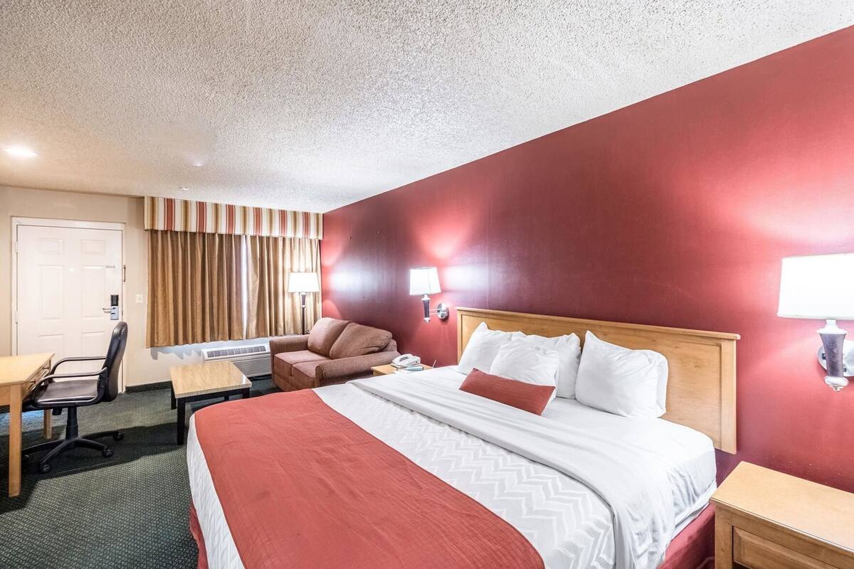 Una habitación de hotel con cama, escritorio, silla y ventana con cortinas.
