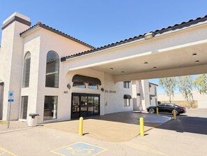 A building with a covered entrance, a sign reading 'ASIAN GRANDE,' and a parking area with yellow bollards.