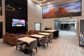 A modern hotel lobby with a large TV screen, comfortable seating, and a scenic wall mural.