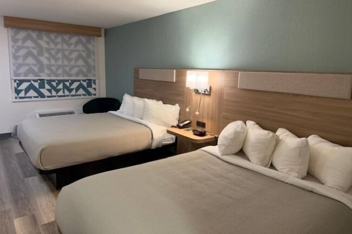 Habitación de hotel con dos camas, una mesita de noche con lámpara, un papel tapiz decorativo y un ventilador de techo.