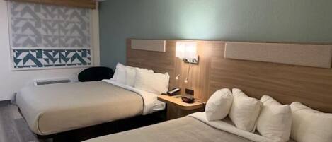 A hotel room with two beds, a nightstand with a lamp, a patterned wall, and a ceiling fan.