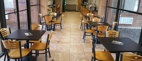 Une cafétéria dotée de nombreuses tables et chaises, d’un espace cuisine et offrant une vue sur l’extérieur grâce à de grandes fenêtres.