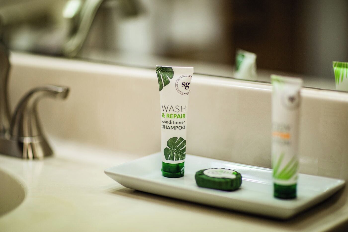 A bathroom sink with a green and white shampoo bottle labeled "WASH & REPAIR conditioner SHAMPOO" and a smaller bottle next to it.