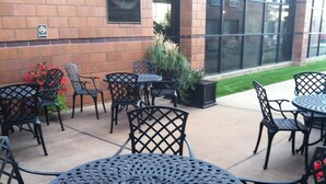 An outdoor patio with metal tables and chairs, a brick wall, and a window with blinds. - Inn at the Canyons (Monticello)