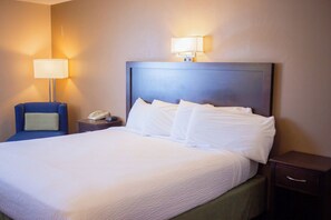 A hotel room with a large bed, a nightstand with a lamp, a chair, and a phone.