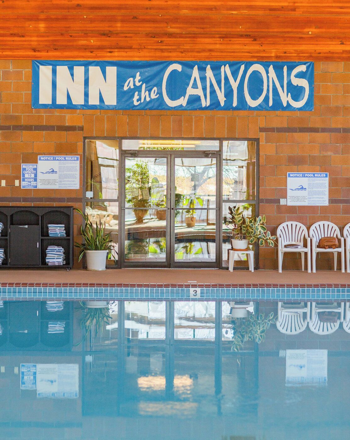 The exterior of the INN at the CANYONS, featuring a pool area with lounge chairs and potted plants.