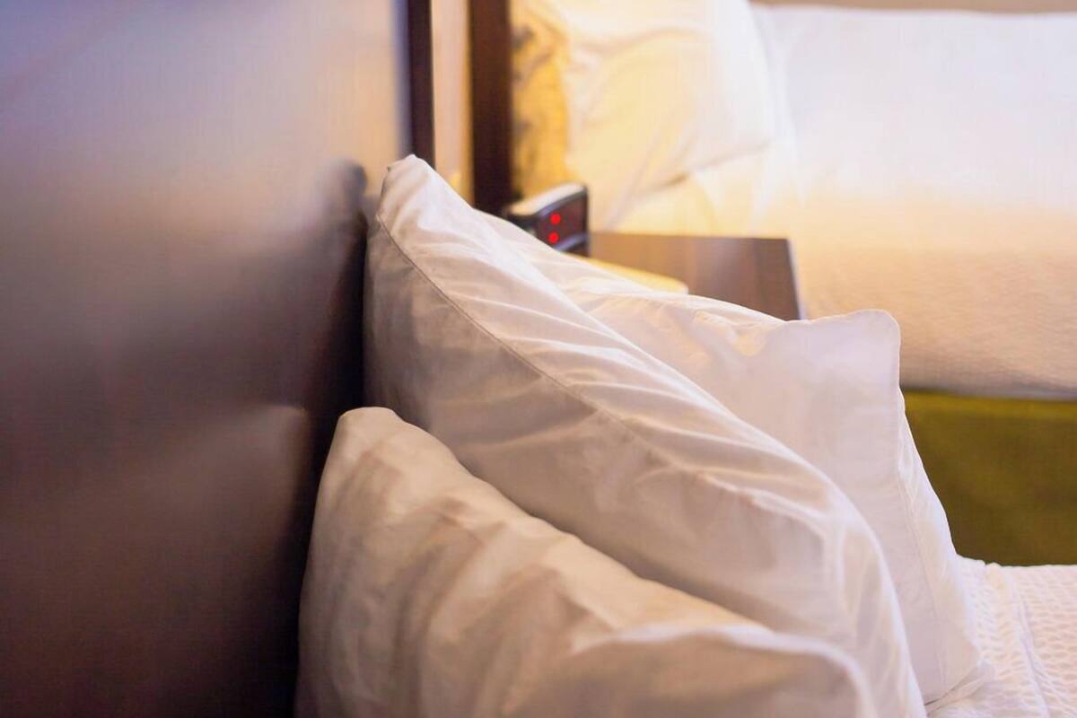 Ein Hotelzimmer mit einem ordentlich bezogenen Bett, weißer Bettwäsche und einer an der Wand befestigten Lampe.