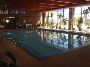 An indoor swimming pool with a wooden ceiling, potted plants, and a sign reading "Inn at the CANYONS".