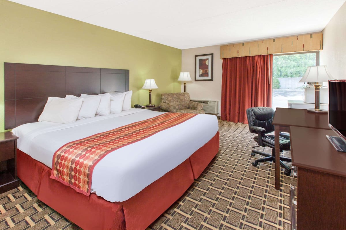 A hotel room with a large bed, a desk, a chair, a lamp, and a window with curtains.
