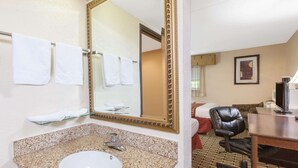 A hotel bathroom with a granite sink, a large mirror, and a chair. - Days Inn & Suites by Wyndham Madison Heights MI (Madison Heights)