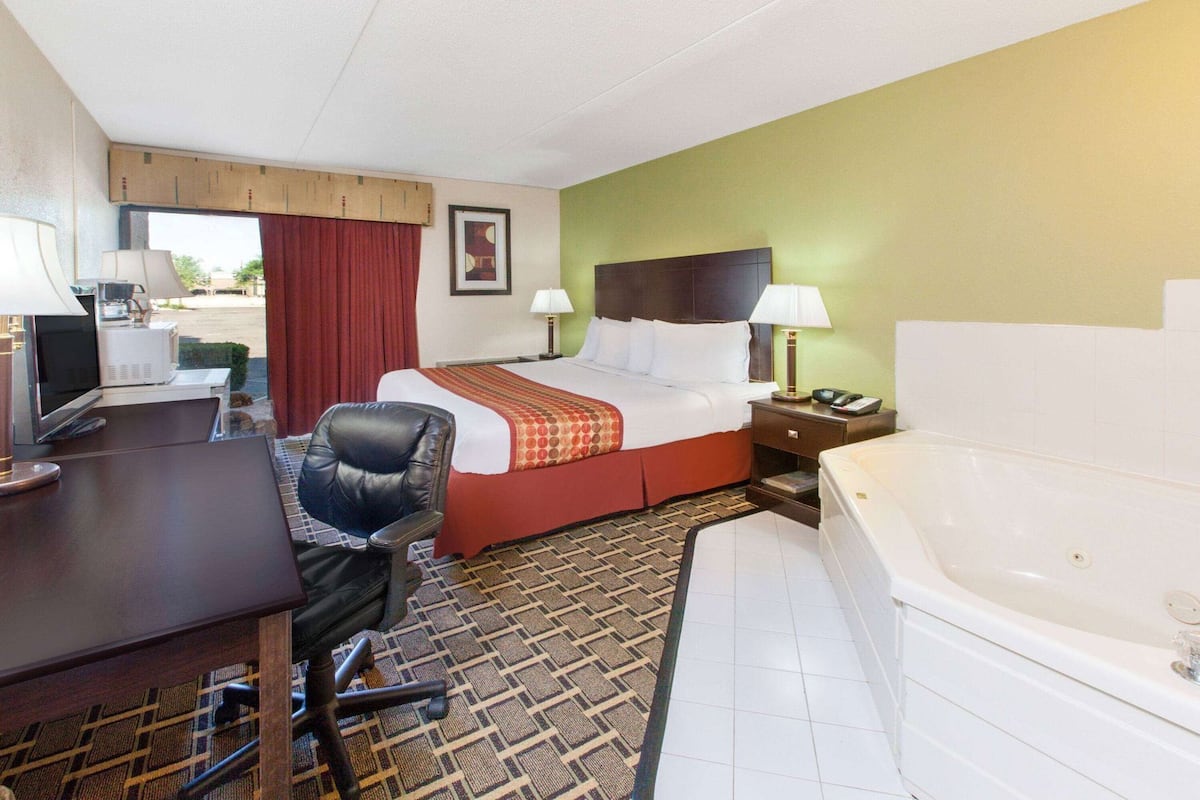 A hotel room with a bed, desk, chair, and a bathtub.