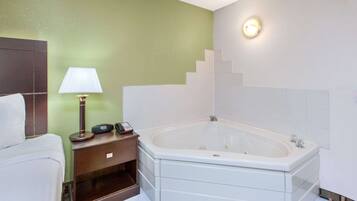 A hotel bathroom with a white bathtub, a bedside table with a lamp, and a green wall.