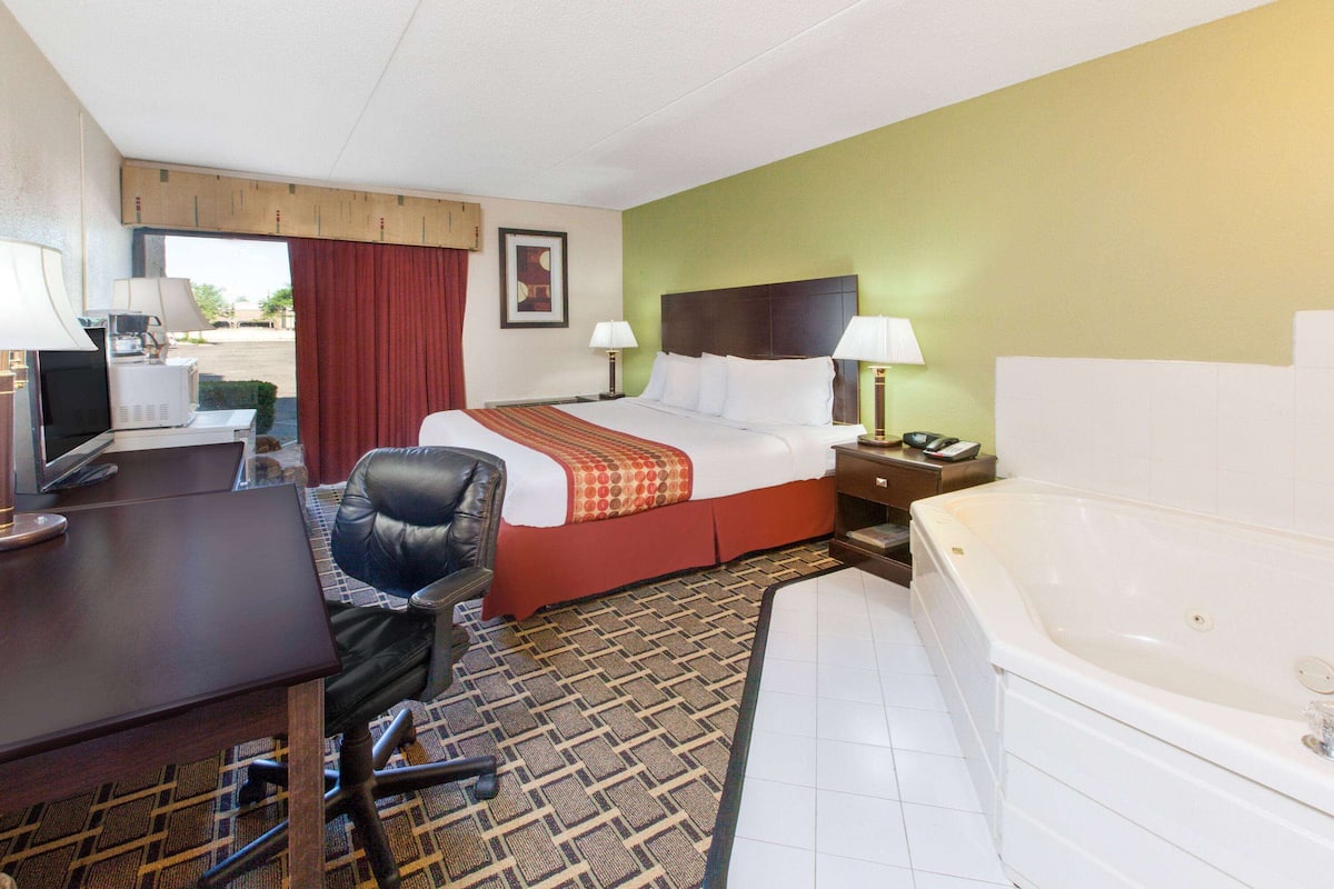 A hotel room with a bed, desk, chair, and a bathtub.