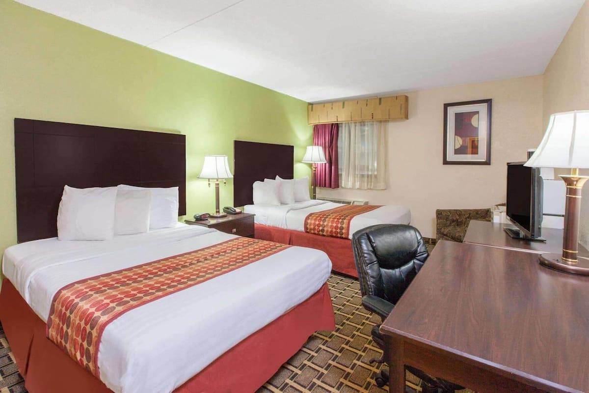 A hotel room with two beds, a desk, a chair, a television, and a window with curtains.