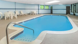 A swimming pool with a tiled edge, a metal handrail, and several white plastic chairs around the pool. - Days Inn & Suites by Wyndham Madison Heights MI (Madison Heights)
