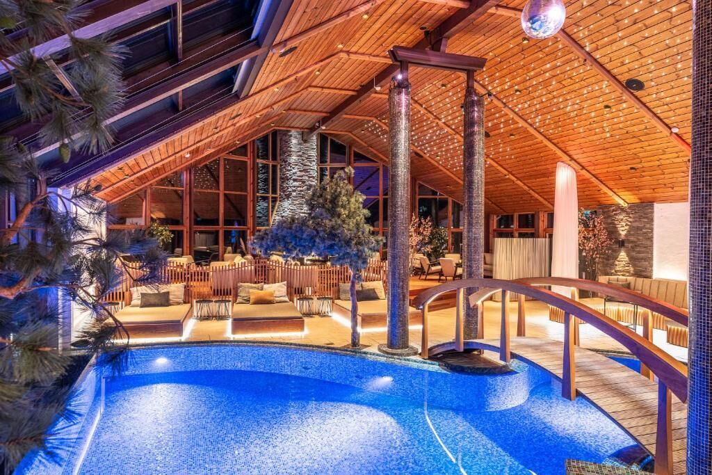 Un área de piscina con techo de madera, un pilar de piedra y una zona de estar con sillas y una mesa.