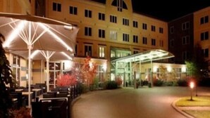En hotelindgang med et overdækket område, brobelagt sti og en bygning med mange vinduer.