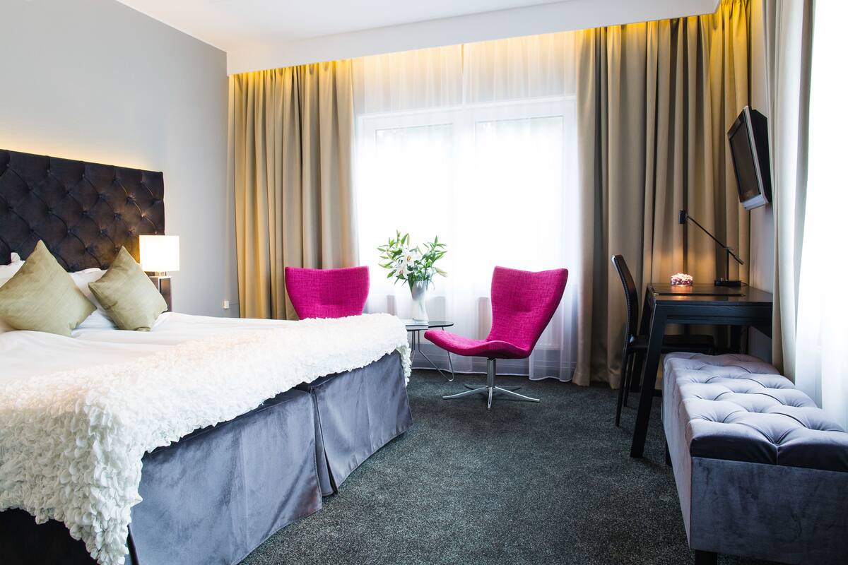 A hotel room with a large bed, a desk, a chair, and a television.
