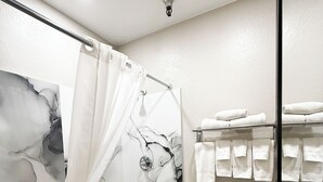 A modern bathroom with a marble shower wall, a white bathtub, a toilet, and a towel rack with folded towels. - Motel 6 Tucson, AZ – Airport / Kino Sports Complex (Tucson)