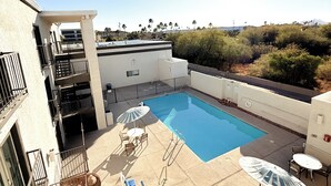 A rooftop pool with a clear blue pool, surrounded by outdoor seating and a view of palm trees and hills. - Motel 6 Tucson, AZ – Airport / Kino Sports Complex (Tucson)