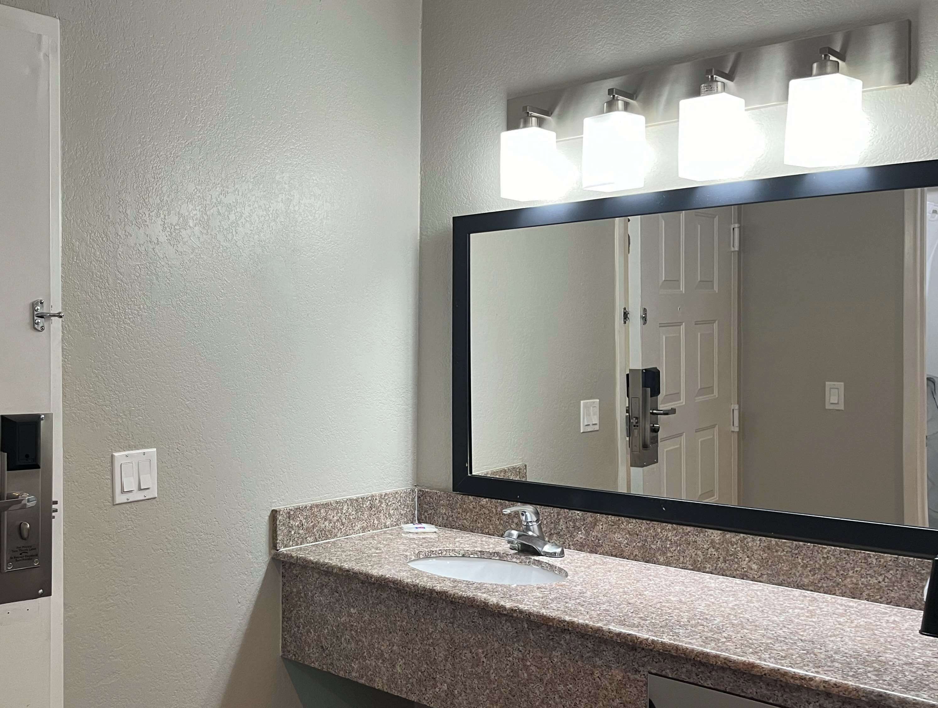 A bathroom with a granite countertop, a sink, a mirror, and a door.