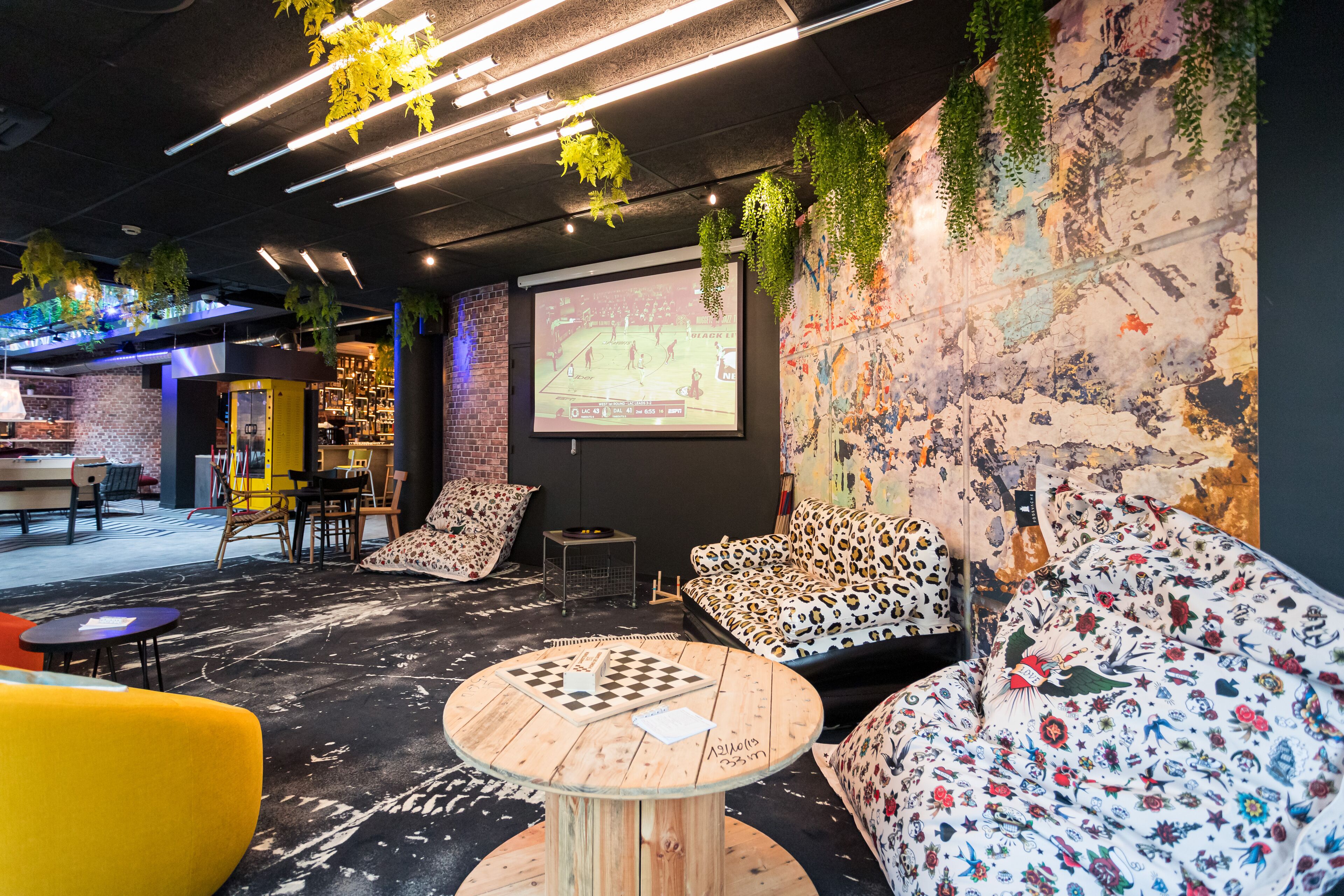 Un espace détente moderne doté d’un grand écran diffusant un événement sportif, de sièges confortables recouverts d’un tissu à motifs floraux et d’une table basse sur laquelle est posé un jeu d’échecs.