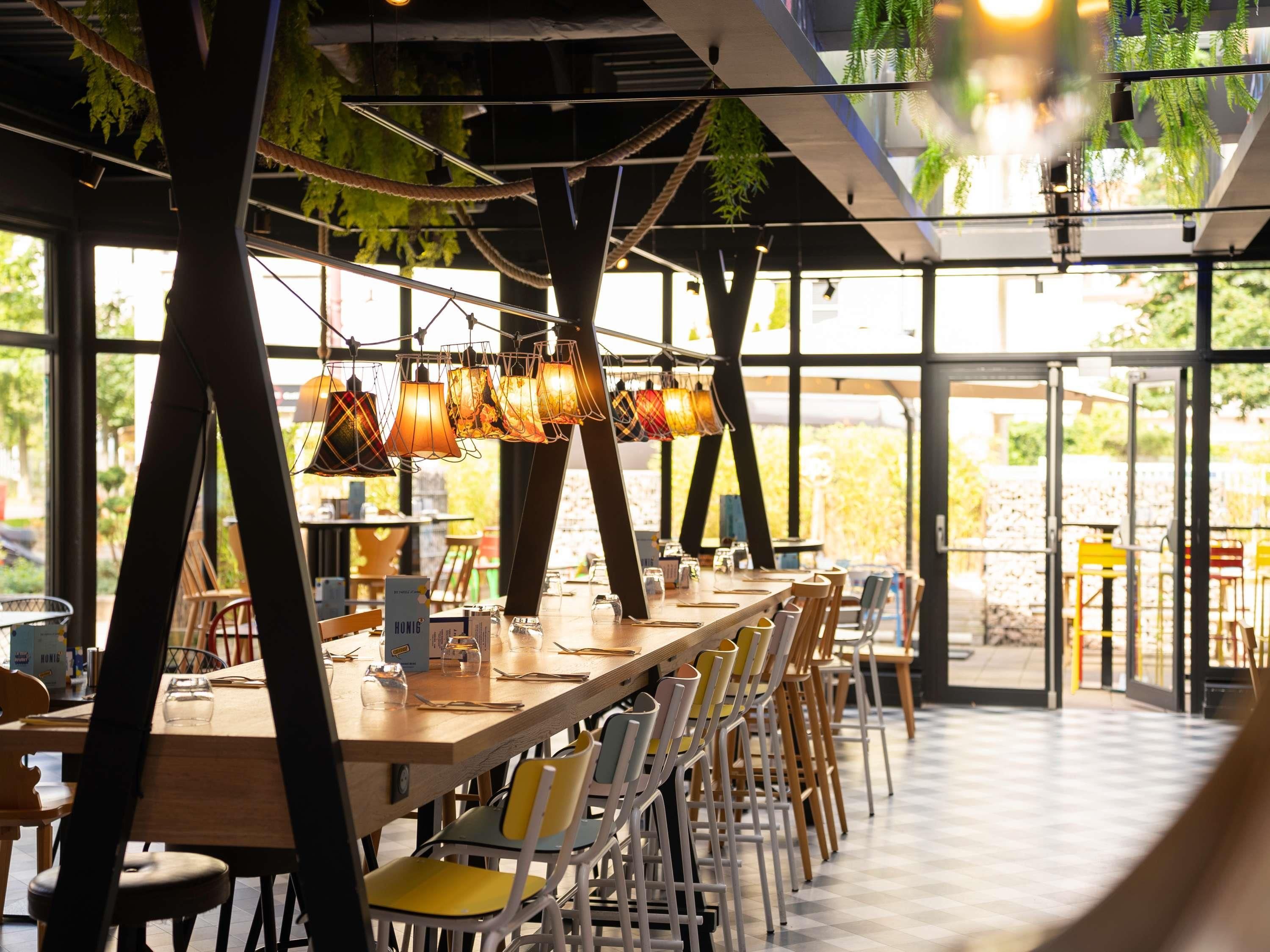 Un restaurant avec une longue table en bois, des chaises jaunes et des lampes suspendues.