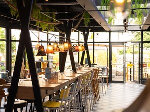 A restaurant with a long wooden table, yellow chairs, and hanging lamps. - ibis Styles Strasbourg Nord Palais des Congrès (Schiltigheim)