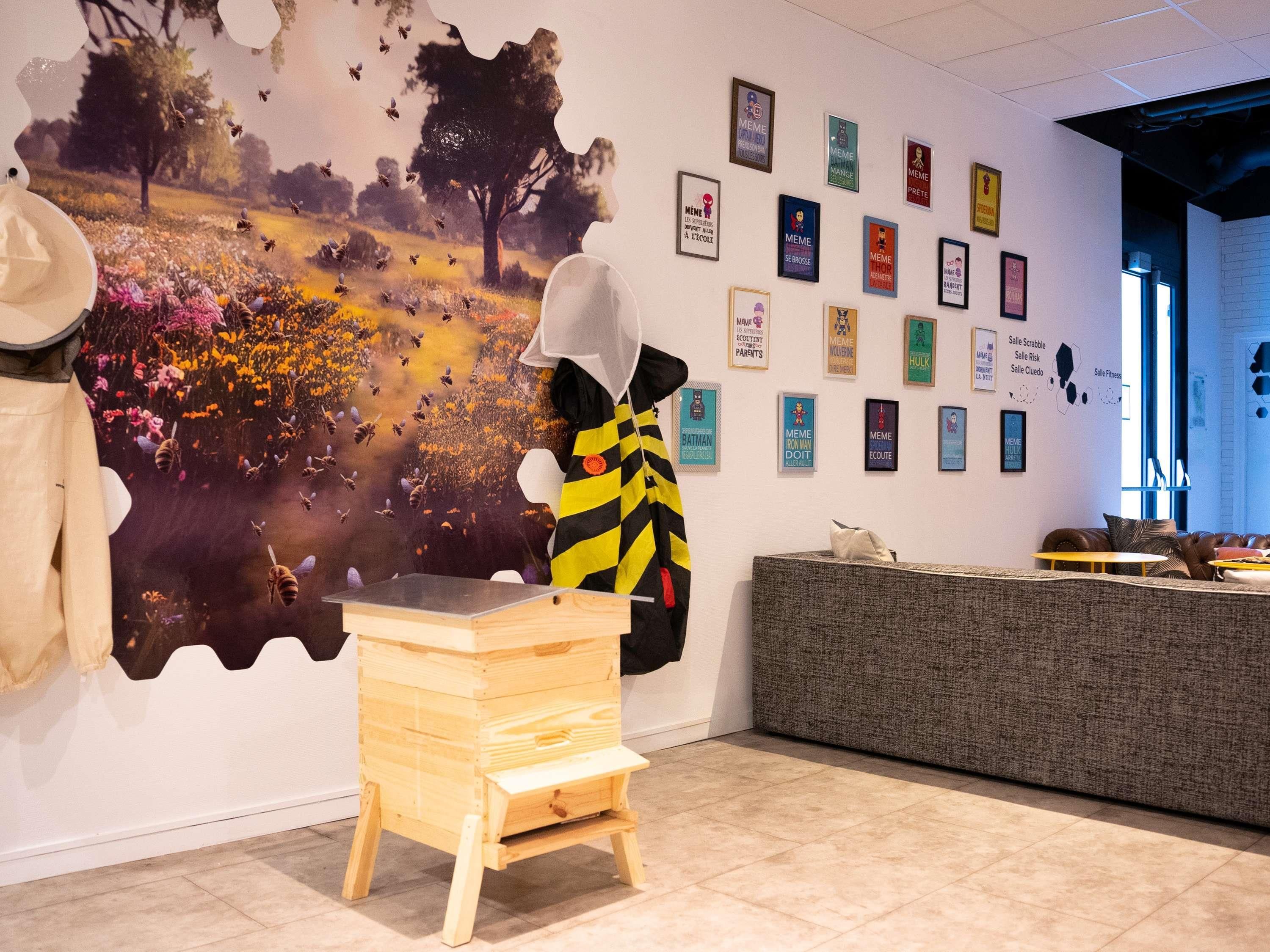 Une pièce avec une fresque murale, un tabouret en bois, un canapé et un mur orné de posters encadrés.