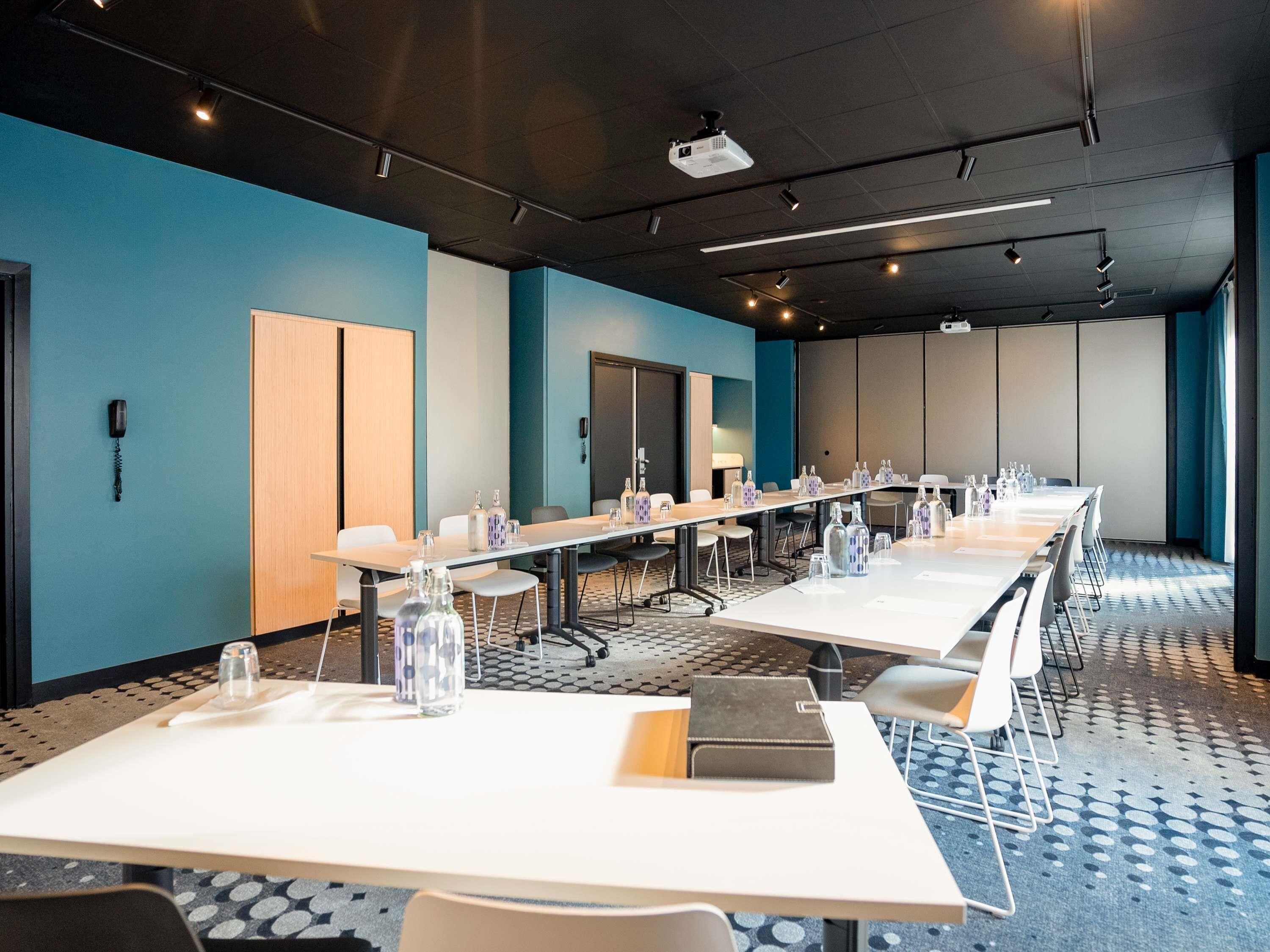 Une salle de conférence équipée de longues tables, de chaises et d’un projecteur.