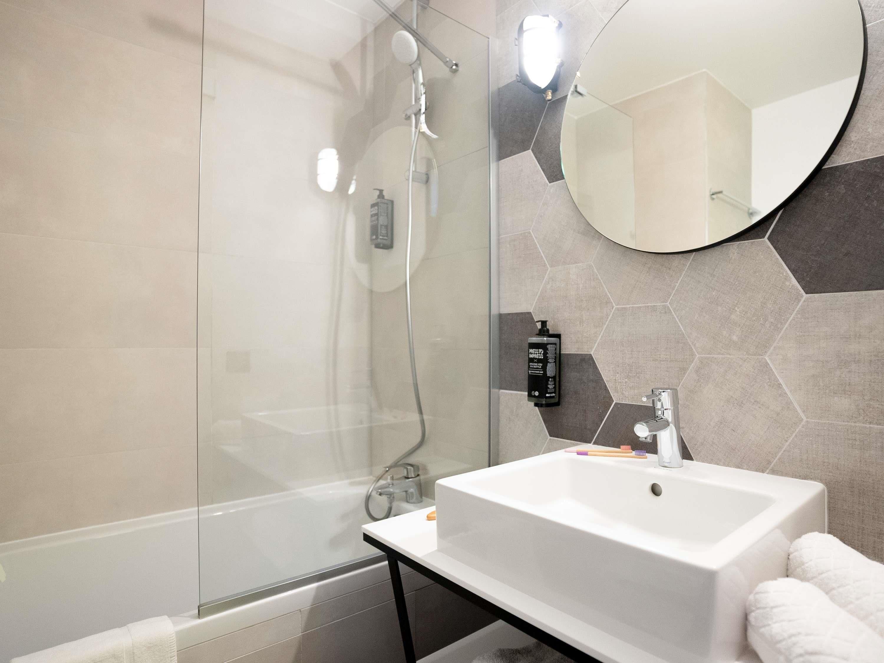 A modern bathroom with a glass shower enclosure, a white sink, and a large mirror.