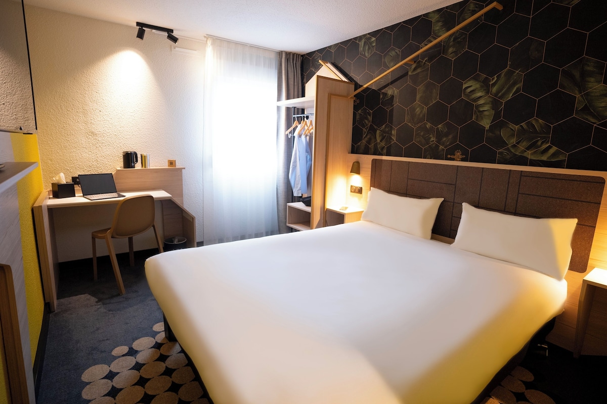 Una habitación de hotel con una cama grande, un escritorio con una computadora portátil, una silla y un armario.