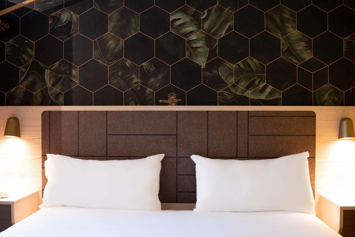 Une chambre d’hôtel avec un lit, deux lampes de chevet et un mur orné d’un motif hexagonal.