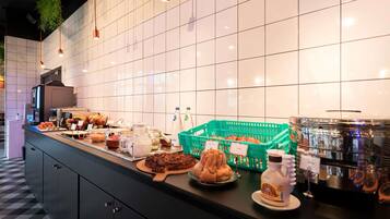 A buffet counter with various food items, a coffee station, and a tiled wall.