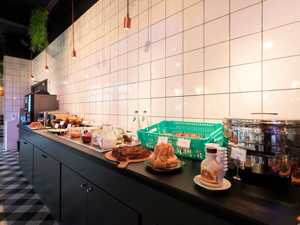 A buffet counter with various food items, a coffee station, and a tiled wall.